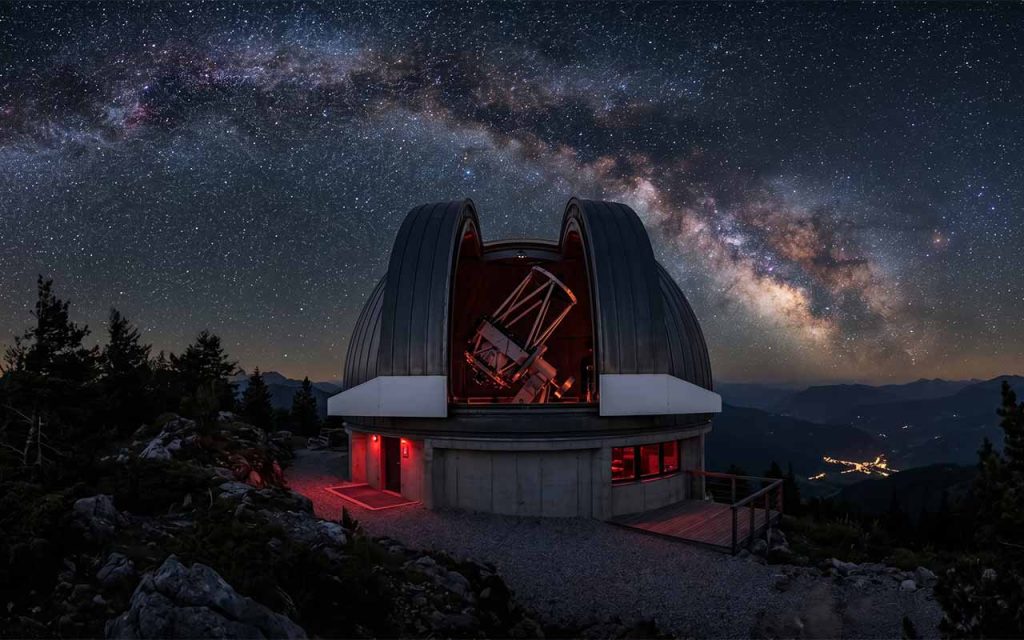 Ein hochmodernes, kuppelförmiges Observatorium bei Nacht, dessen Teleskop durch einen geöffneten Spalt in den sternenklaren Himmel gerichtet ist.